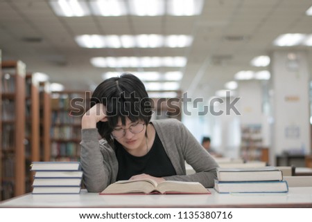 stressed asian student girl with glasses reading books in the library