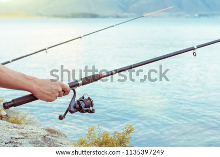 hand with spinning and reel on summer lake. two fishing rods catching fish
