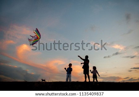 Happy family on the field. Father and kids playing with a kite while running on meadow, sunset, in summer day. Funny family time. Happy little childs launch a kite with dad.