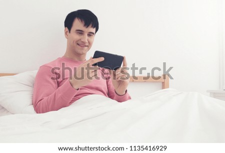 Happy man sitting on bed and watch movie on phone at home in the bedroom