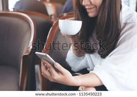 Closeup image of an asian woman holding , using and looking at smart phone while drinking coffee in cafe