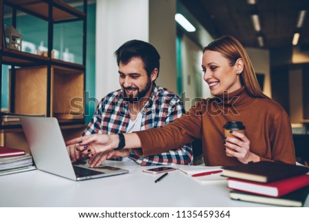 Cheerful internet users laughing and enjoying time after watching webinar online at coworking space, smiling friends sitting at cafeteria and communicated via laptop while girl holding cup coffee Royalty-Free Stock Photo #1135459364