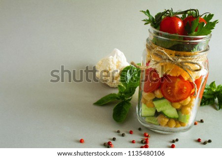 Vegetarian salad with vegetables and chickpea  in the glass jar on the  grey  background