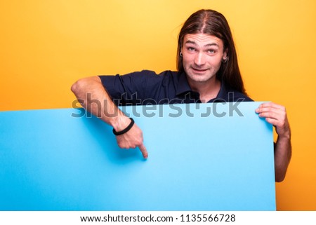 Portrait of positive smiling man pointing finger to a cardboard. Expresion positive of male shot in a studio on orange background