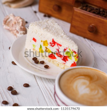 Cake with colored jelly on a table with a cup of cappuccino and shells.