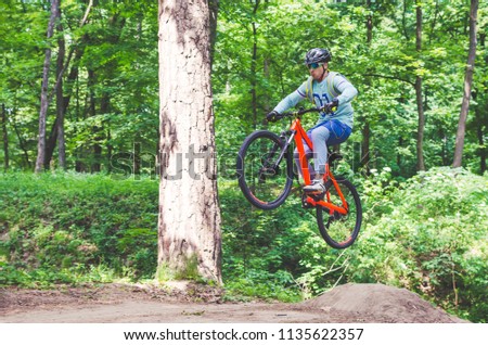 Cyclist in helmet on an orange bike doing a trick in a springboard jump in the forest, motion blur.