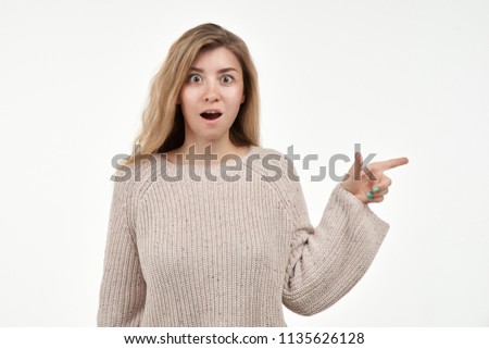 Portrait of astonished attractive young woman with index finger shows to the side, keeps her mouth wide open, shows something amazing for your advertising. People and reaction.