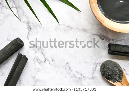 Facial mask and scrub by activated charcoal powder on marble table. Free space for text Royalty-Free Stock Photo #1135717331