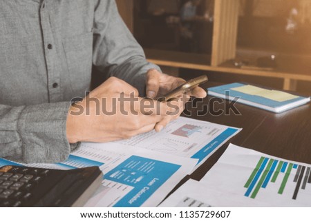 Accountant working on his wooden table in the office with smart phone,calculator,document and notebook in business, Savings, finances and economy concept.