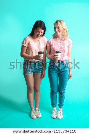 Portrait Couple of multiracial girlfriends looking at camera while holding takeaway coffee cup isolated over studio blue background