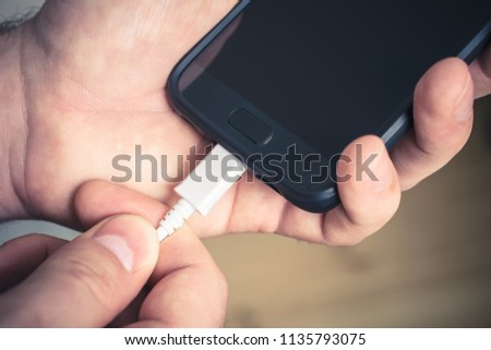 Plugging Out A White USB Cable Connected With A Black Mobile Phone, Holded By Male Hands