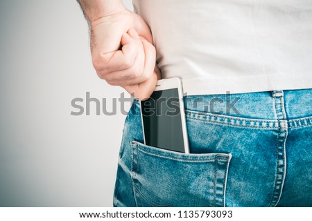Male Hand Grabbing A Smartphone In The Left Back Pocket Of A Jeans Trouser Royalty-Free Stock Photo #1135793093