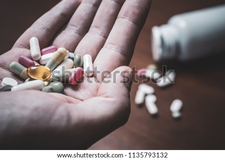 Macro Of A Male Hand Holding Several Pills With Prescription Bottle And More Pills In Background - Taking Too Many Pills Concept Royalty-Free Stock Photo #1135793132
