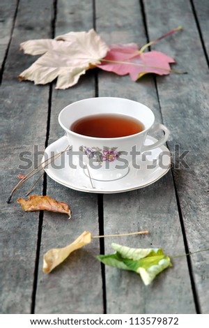 A white vintage cup of tea on grey rustic wooden table, with colorful autumn leaves. Royalty-Free Stock Photo #113579872