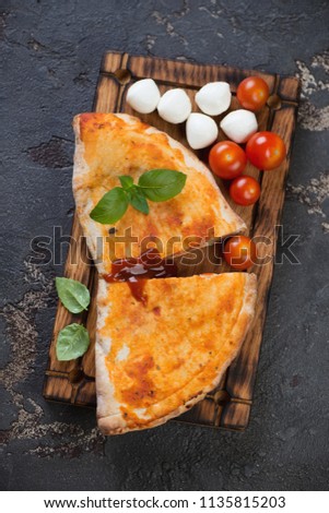 Sliced italian pizza calzone on a rustic wooden serving tray, flatlay on a brown stone background, vertical shot