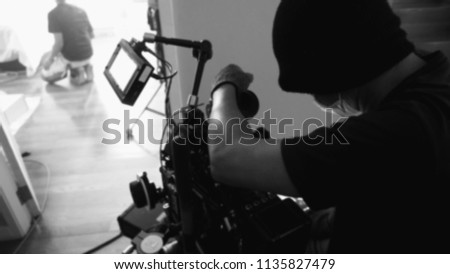 Blurred image of video camera high definition on pan and tilt head professional tripod with rig and gimbal operated by film crew team that recording or shooting tvc movie at location with monitor.