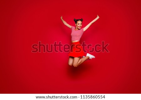 Full-length full-size view of jumping laughing and happy woman dressed in colourful bright clothes isolated on red background