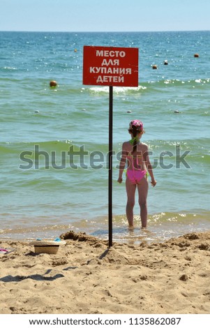 Girl in pink bathing suit goes to bathe in sea in specially designated place for 
bathing children. Inscription on plate: "Place for bathing children"