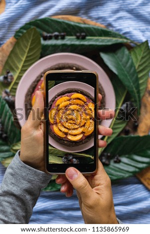 Smartphone food photography of vegetarian dessert. Raw vegan pie or tart with fruits. Woman hands taking phone photo of food in trendy style for social media or blogging.