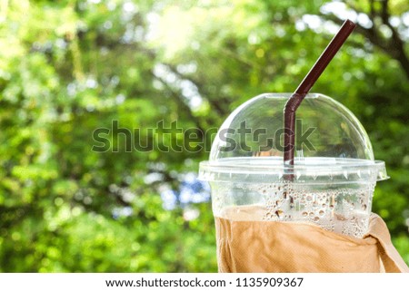 An empty iced coffee in plastic glass with brown straw with light bokeh green, yellow nature background