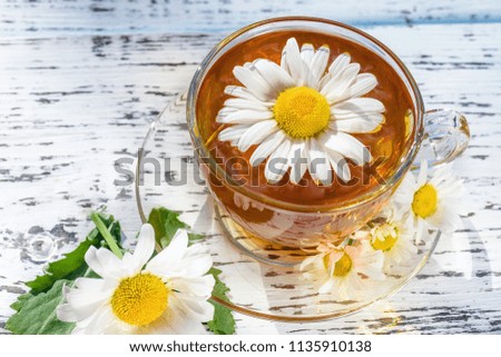 A cup of tea with chamomile, close-up, lit by sunlight, on a white wooden table.