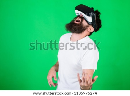 Guy with VR glasses learn to play music on guitar. VR musician concept. Man with beard in VR glasses, green background. Hipster guitarist on enthusiastic face use modern technology for entertainment.