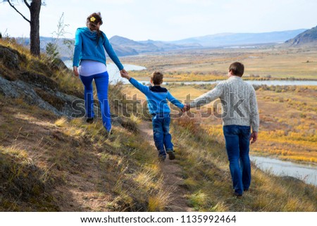 A happy family, father and mother and son, are walking along the slope of the mountains in the direction of the valley below and the floodplain of the river