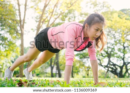 Asian young woman warm up her body by push up to build up her strength before morning jogging exercise and yoga on the grass under the warm light sunshine in the morning. Exercise outdoor concept.