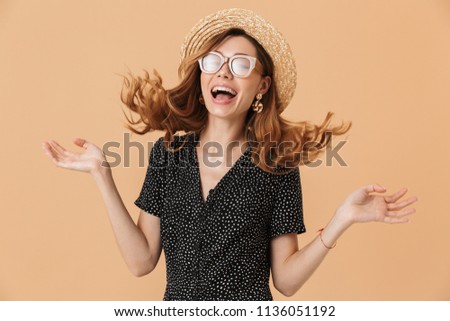 Portrait of happy cute woman 20s wearing straw hat and sunglasses laughing with shaking hair isolated over beige background