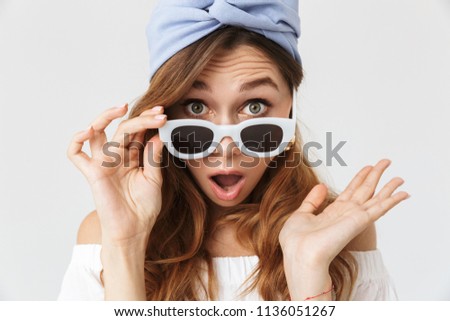 Portrait closeup of excited pretty woman 20s looking at camera from under sunglasses isolated over white background
