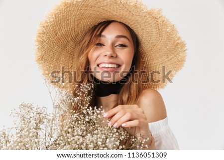 Portrait of joyful brunette woman 20s wearing big straw hat looking at you with happy smile and holding field flower isolated over white background