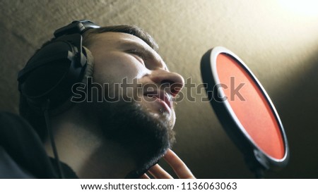 Male singer in headphones singing song into the microphone at sound studio. Young man emotionally recording new song. Working of creative musician. Show business concept. Slow motion Low angle of view