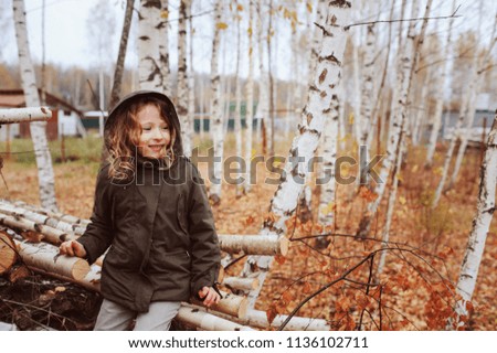 happy kid girl sitting on birch wood stack in autumn forest