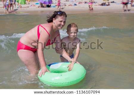 Mom and son are swimming in the sea.Young mother in bikini standing swimming and playing with male child boy in sea or ocean water sunny day outdoor on natural background, horizontal picture