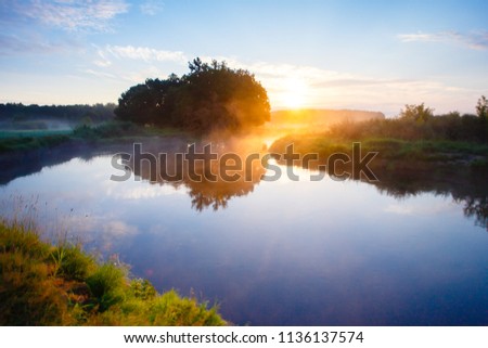 Foggy summer morning at bright sunrise over the river. Daybreak landscape