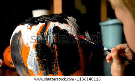 Young boy carving and painting a pumpkin for Halloween on a table