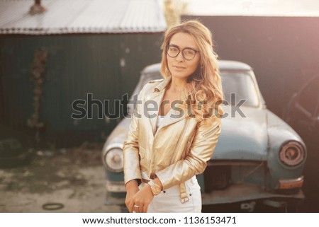 a beautiful blonde with long hair in white denim shorts stands near an old retro car