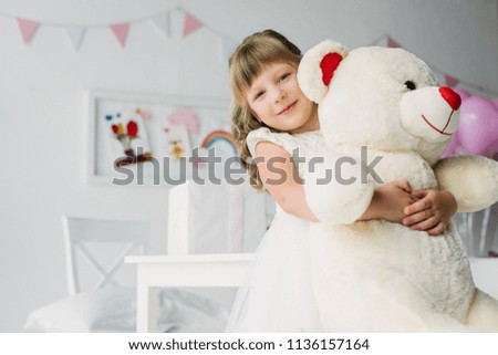 happy birthday kid in white dress embracing teddy bear