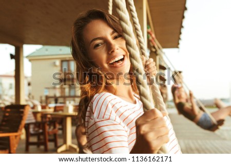 Picture of happy young lady outdoors on the beach riding on swing.