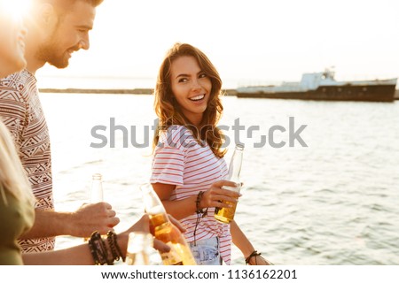 Picture of happy young friends outdoors on the beach drinking beer.