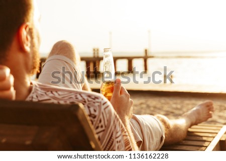 Picture of handsome man have a rest outdoors on the beach drinking beer.
