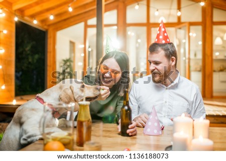 Funny dog with young couple sitting at the table during a celebration on the backyard of the house outdoors