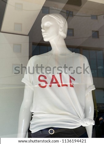 Female Mannequin in shop window. On the dummy is wearing a white T-shirt on which is written in red color sale.