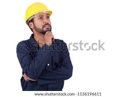 Close shot of a handsome repairman wearing a helmet for safety and an overall, he is thinking about something putting his hand on chin and looking up, isolated on white background.
