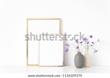 Gold portrait a4 and a5 frame mockup with wild lilac bellflower in vases near wall on white background. Empty frame mock up for presentation design. Template framing for modern art.