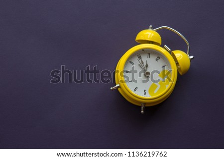 Cute small yellow ring alarm clock on bright purple background