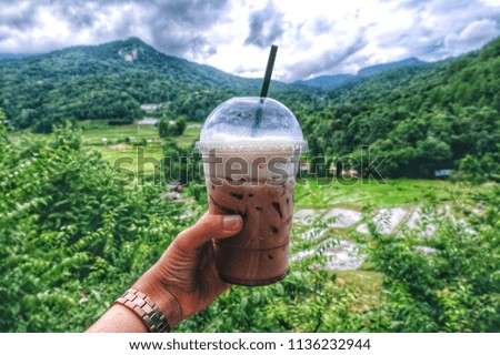 a plastic cup of cocoa drink up to the top in natural mountain rice field in water green background