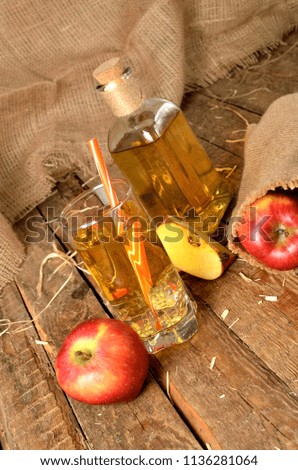 Apple juice, red apples, straw and bottle in background on rustic wooden boards