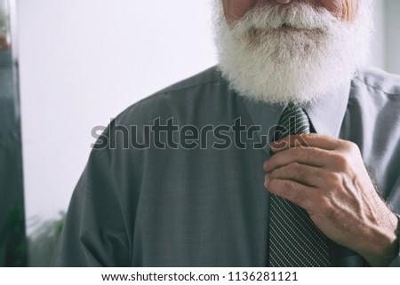 Cropped image of aged bearded entrepreneur adjusting necktie