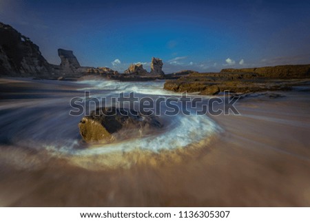 Beautiful beach in long exposure shot with motion blur of silky waves around the rocks and beautiful blue sky background